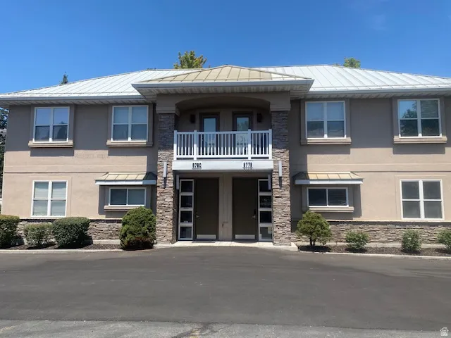 Two-story exterior featuring a metal roof, stucco siding, and stone veneer accents