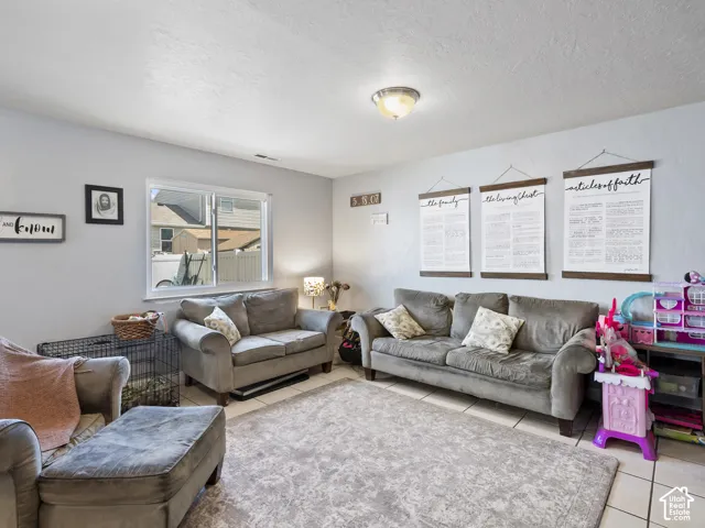 Spacious living area featuring light-toned walls, tile flooring, and a large window providing ample natural light