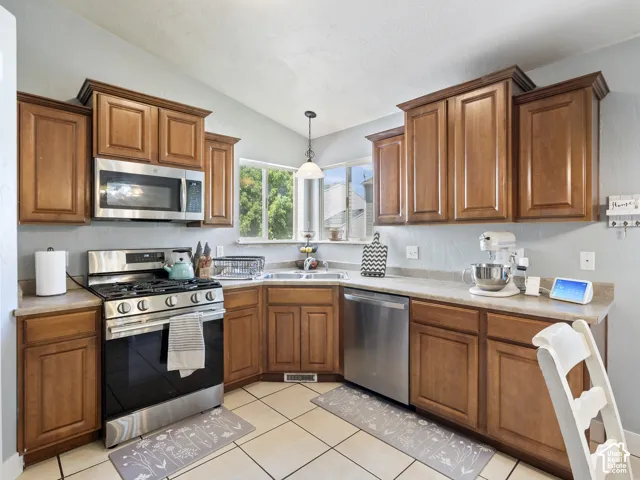 Kitchen featuring wood-finish cabinetry, stainless steel appliances, and a vaulted ceiling