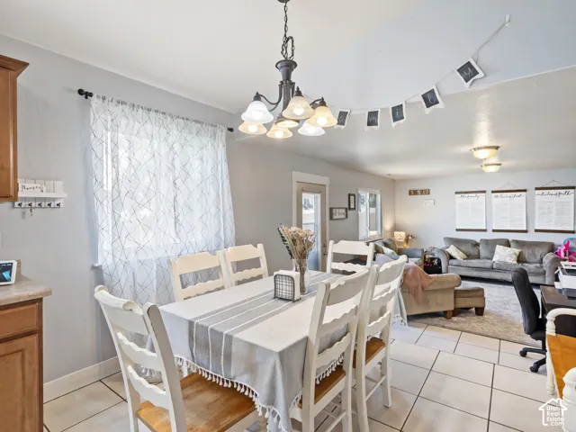 Dining area featuring a chandelier with frosted glass shades, a window with sheer curtains, and tile flooring