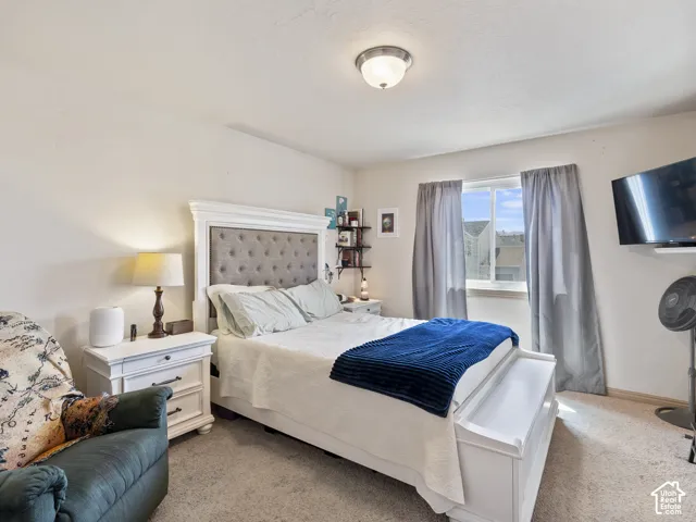 Carpeted bedroom featuring a window with natural light, a ceiling-mounted light fixture, and a built-in wall shelf