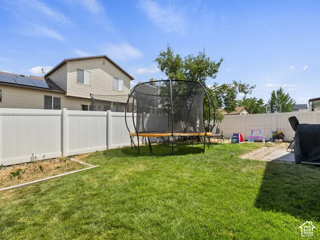 Expansive backyard featuring a green lawn, white vinyl fencing, and a concrete patio space