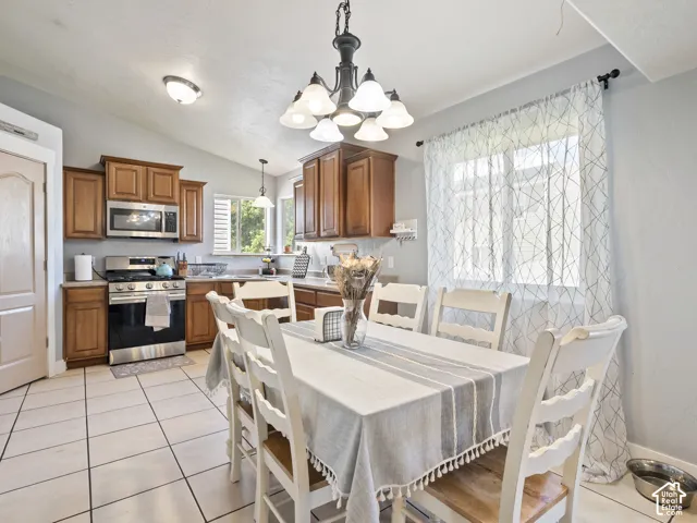 Open-concept kitchen and dining area featuring light wood-finish cabinetry, stainless steel appliances, and white tile flooring