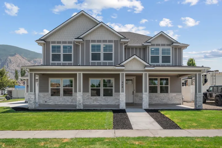 Newly constructed residence featuring a covered front porch with stone-clad columns and a gray siding exterior