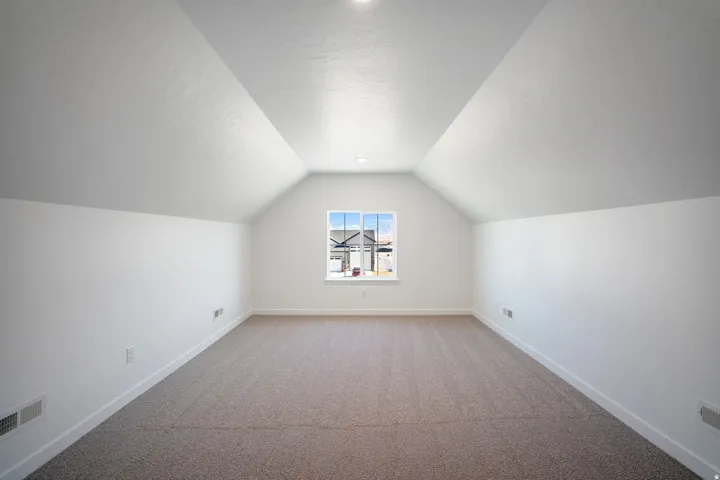 Spacious room featuring vaulted ceilings, a central window, recessed lighting, white walls, and neutral carpeting