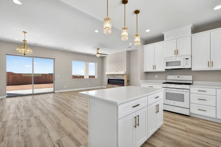 Spacious kitchen featuring an expansive island with a pristine countertop, white cabinetry with brushed bronze hardware, and pendant lighting