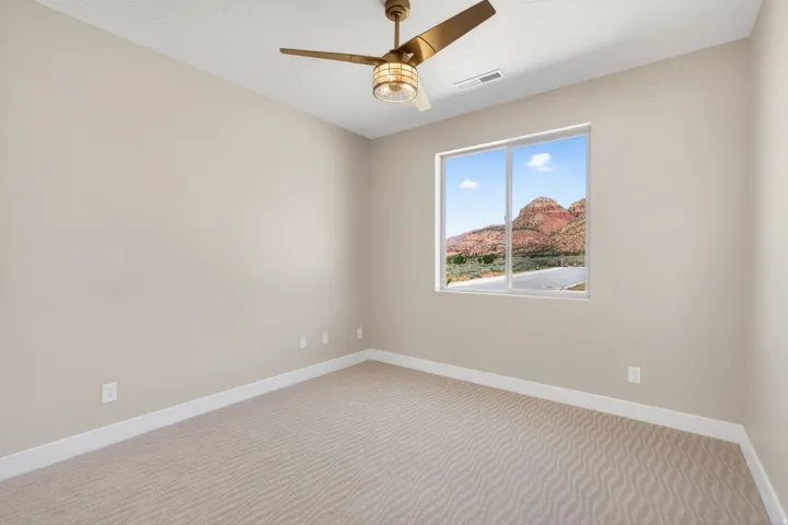 Spacious room featuring neutral-toned walls, patterned carpet flooring, a contemporary ceiling fan with integrated lighting, and a large window offering mountain scenery