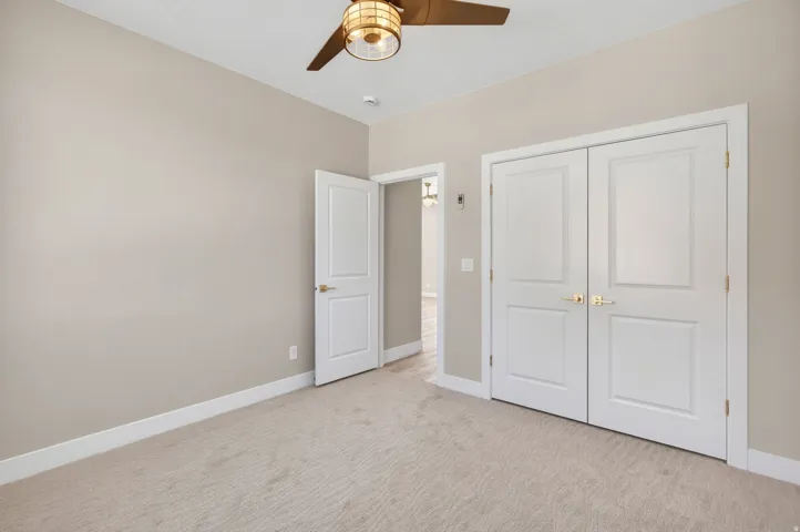 Carpeted room featuring a ceiling fan with integrated lighting, a single paneled door, and double paneled doors with brass hardware