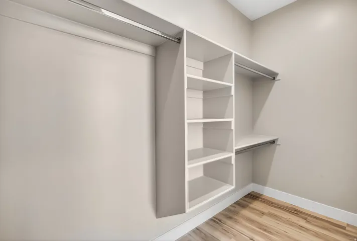Walk-in closet featuring built-in shelving, multiple hanging rods, and wood-finish flooring