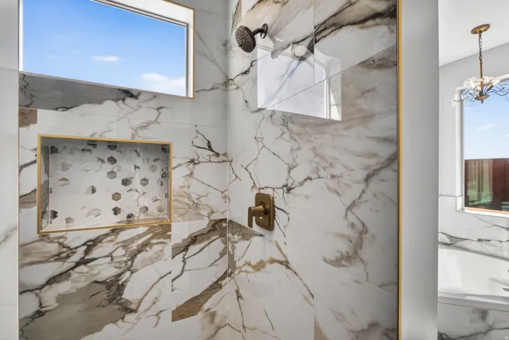 Shower featuring large-format marbled tile, a built-in shower niche with mosaic tile inlay and gold-tone trim, a bronze-finish showerhead, and a bronze-finish control lever