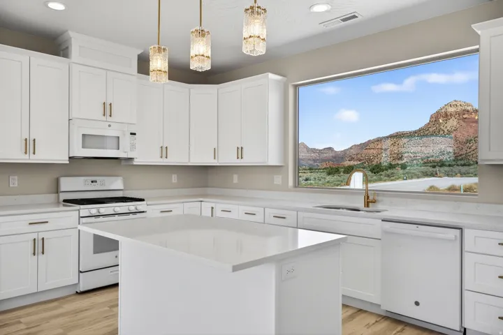 Bright kitchen featuring white cabinetry, a large picture window, a central island with a solid surface countertop, wood-finish flooring, and pendant lighting fixtures