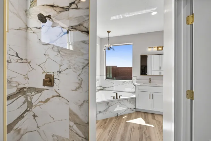 Spacious bathroom featuring a glass-enclosed shower with large format marble-look tile, a separate built-in soaking tub, wood-finish flooring, a white vanity with a rectangular sink, and a built-in medicine cabinet