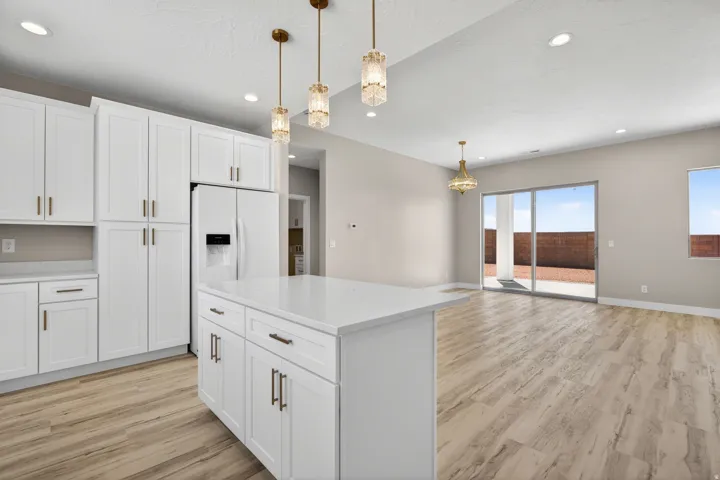 Open-concept kitchen and living area featuring white shaker cabinetry, an island with a light-toned countertop, and wood-finish flooring