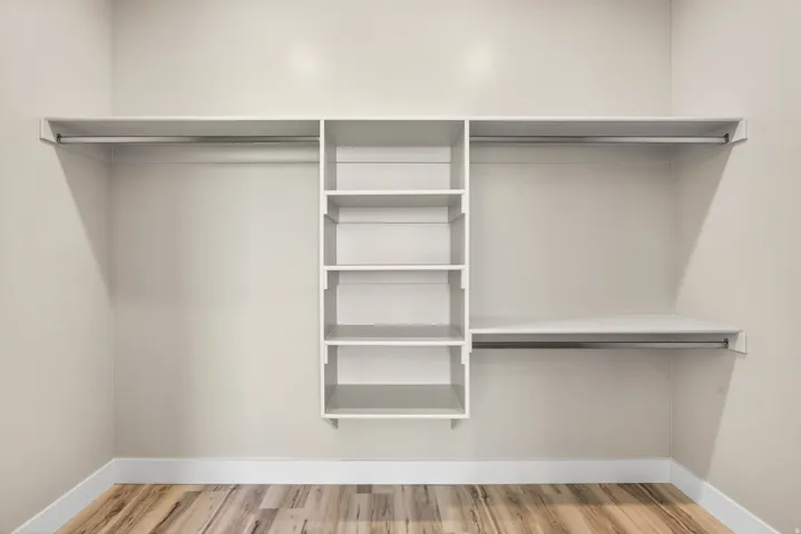 Custom closet system featuring multiple hanging rods, integrated shelving units, and wood-finish flooring