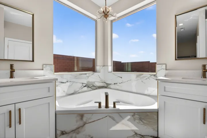 Freestanding soaking tub with a surrounding marble-finish enclosure, dual rectangular windows, and a brass-tone chandelier