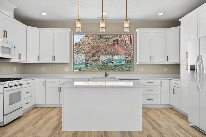 Modern kitchen featuring white cabinetry, a center island with a sink, stainless steel appliances, wood-finish flooring, and pendant lighting