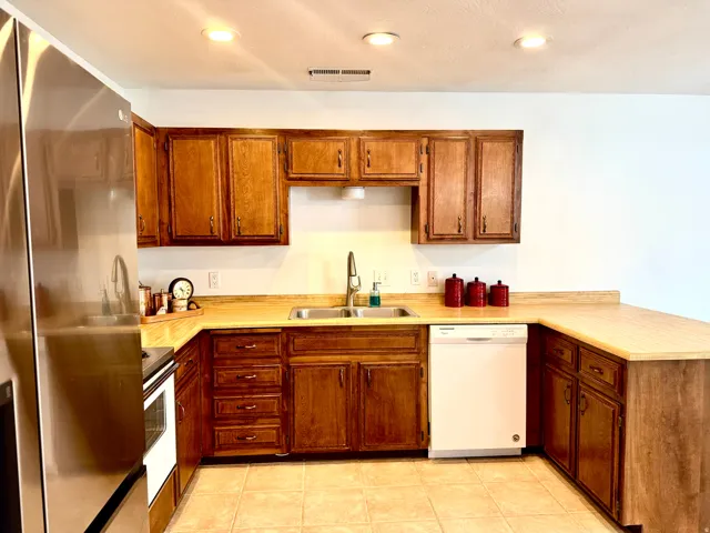 Kitchen featuring wood cabinetry, tan countertops, a double basin sink with a high-arc faucet, integrated dishwasher, and tile flooring