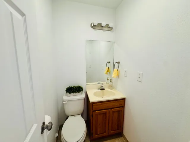 Compact bathroom featuring a white toilet, wood-finish vanity with an integrated sink, and a wall-mounted mirror