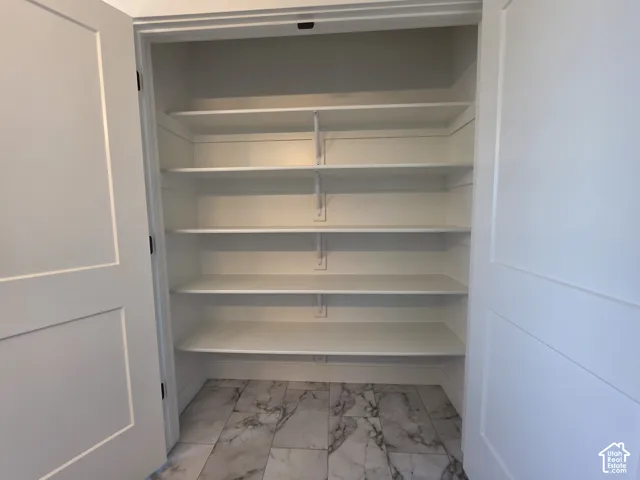 Built-in storage closet featuring multiple white shelves, a tile-finish floor, and white paneled doors
