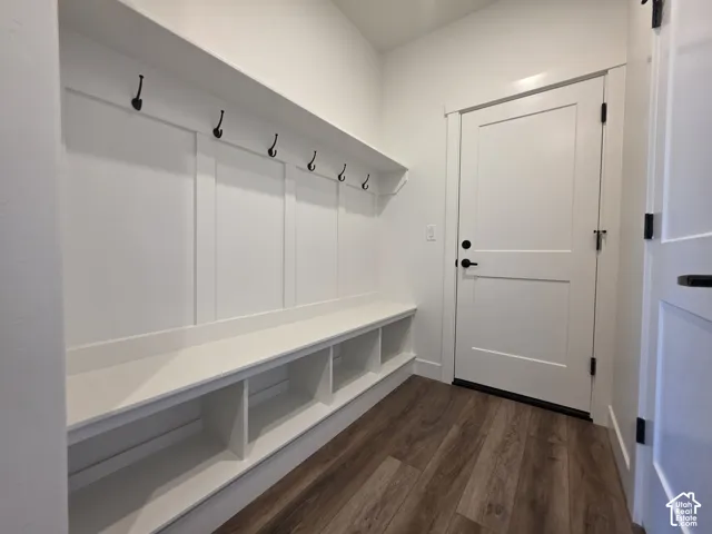 Entryway featuring wood-finish flooring, white paneled millwork with integrated bench seating, built-in storage cubbies, matte black coat hooks, and a white panel door with matte black hardware