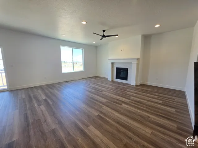 Expansive room featuring wood-finish flooring, a contemporary fireplace with white tile surround, a large window, recessed lighting, and a ceiling fan