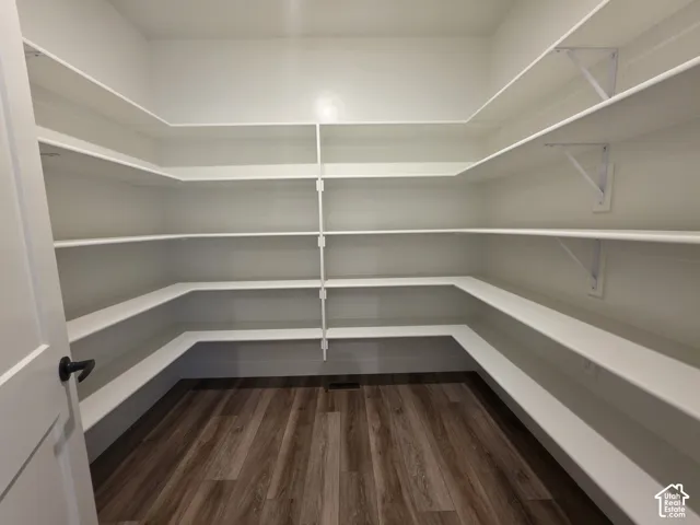 Spacious walk-in pantry featuring extensive white shelving, dark wood-finish flooring, and a white interior door with matte black hardware