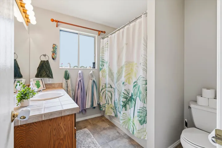 Bathroom featuring a wood-finish vanity with a tile countertop, integrated sink, and tub/shower combo