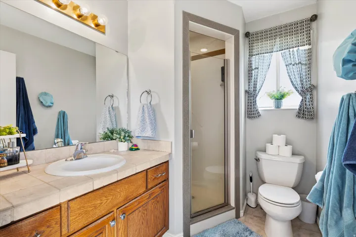 Primary Owner's Bathroom featuring a wood-finish vanity with a tiled countertop and an integrated sink, a glass-enclosed shower, and a privacy window