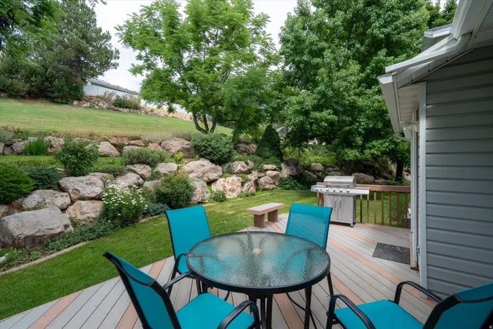 Expansive multi-level backyard featuring a composite deck, mature trees, and a rock retaining wall with established landscaping