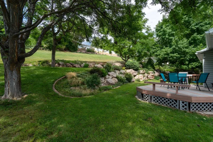 Expansive backyard featuring a multi-level rock garden, mature trees, and a spacious composite deck with lattice skirting