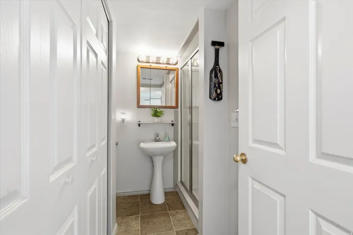 Bathroom featuring a pedestal sink, wood-framed medicine cabinet with integrated lighting, toilet  and a glass-enclosed shower