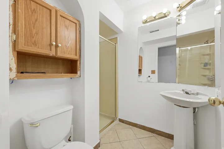 Bathroom featuring a pedestal sink, wall-mounted mirror with overhead lighting, and a walk-in shower with a glass enclosure