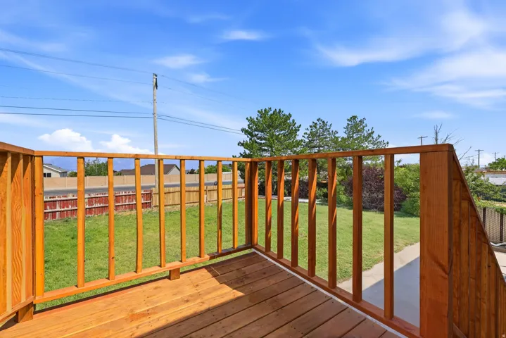 Outdoor deck with wood-finish railing and decking, overlooking a fenced backyard with green lawn