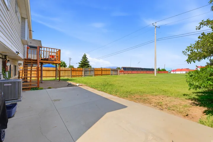 Expansive backyard featuring a large concrete patio, a multi-level wood deck, a wood privacy fence, and a spacious grassy area