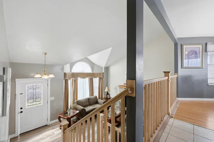 Vaulted ceilings with a prominent arched window, wood-finish flooring, and a decorative front entry door featuring leaded glass accents