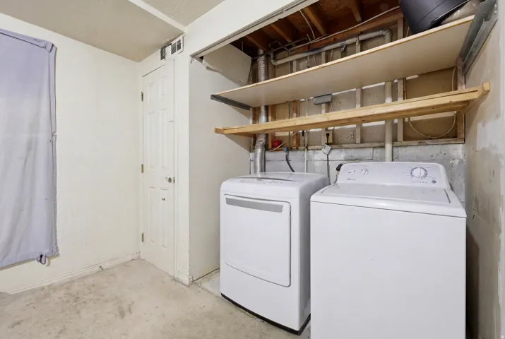Dedicated utility area featuring concrete flooring, an overhead light fixture, and two built-in wood shelves