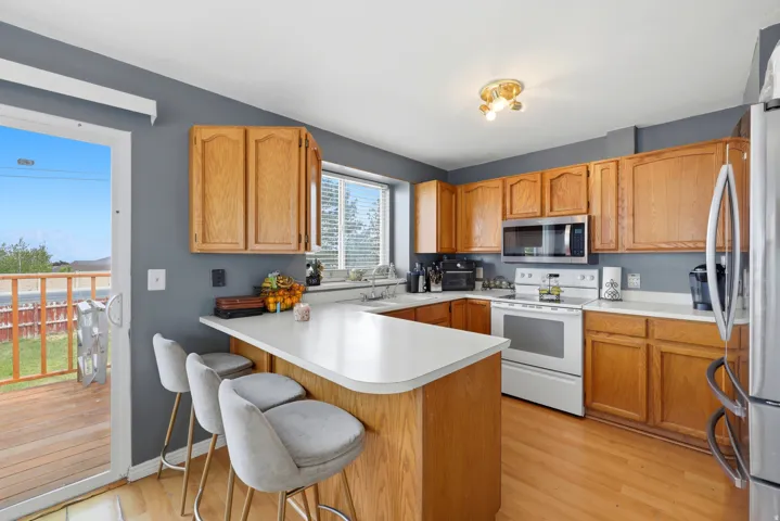 Kitchen featuring wood-finish flooring, light wood cabinetry, white countertops, and a full suite of appliances including a range, microwave, and refrigerator