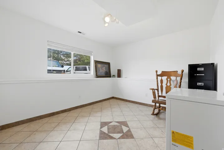 Spacious room featuring tile flooring with a decorative inlay, clean white walls, and a large window with white blinds