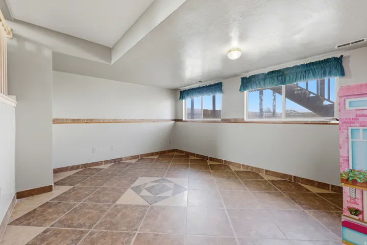 Spacious room featuring large format tile flooring with a decorative center inlay, white walls with a tile wainscoting accent, and two windows providing natural light