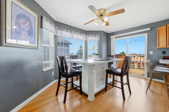 Dining area featuring wood-finish flooring, bay windows with blinds, a ceiling fan, and direct access to an outdoor deck through a sliding glass door