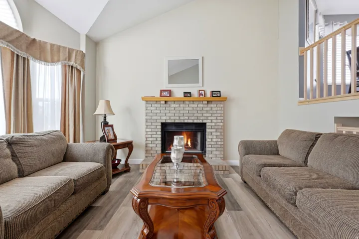 Living area featuring a brick fireplace with a wood mantel, vaulted ceilings, and wood-finish flooring