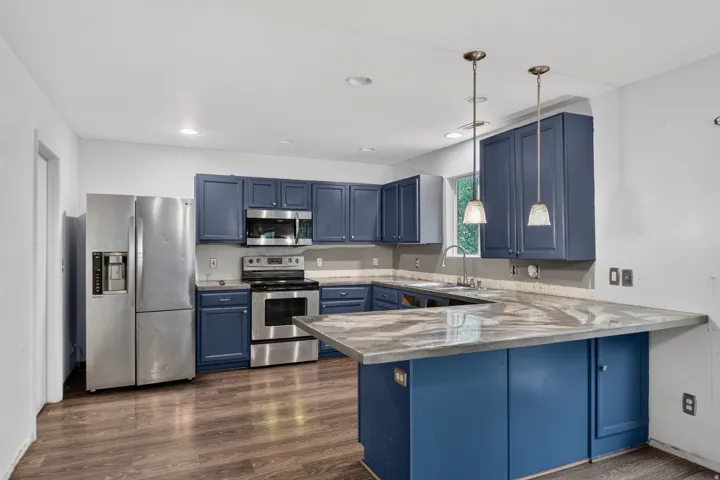 Kitchen featuring blue cabinetry, stainless steel appliances, wood-finish flooring, and a patterned countertop with a breakfast bar