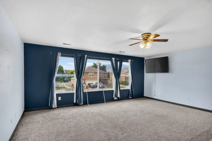 Spacious room featuring multiple large windows, a ceiling fan with integrated lighting, and neutral carpeting
