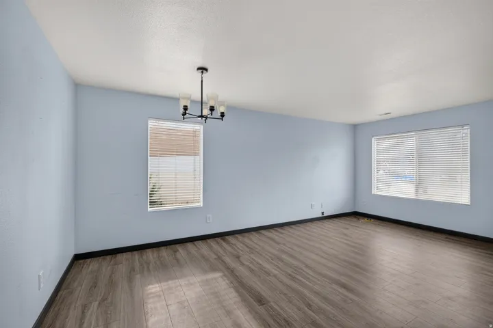 Spacious room with wood-finish flooring, light blue walls, and multiple windows with blinds