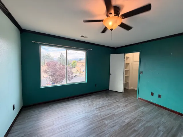 Room featuring wood-finish flooring, a ceiling fan with integrated lighting, and a window with a neighborhood perspective