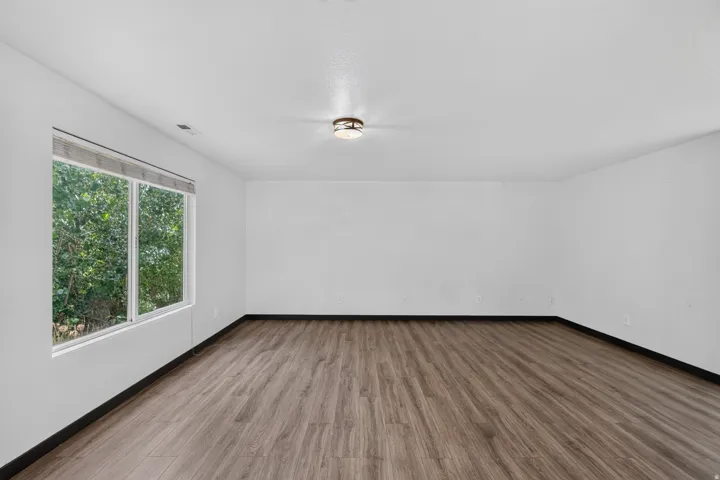 Spacious room featuring wood-finish flooring, white walls, and a large window with natural outdoor scenery