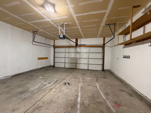 Spacious garage featuring a concrete floor, overhead lighting, an automatic garage door opener, and built-in shelving for storage