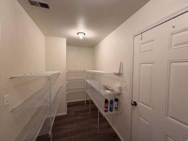 Ample storage room featuring wood-finish flooring, white walls, and a ceiling-mounted light fixture