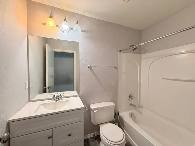 Bathroom featuring a white vanity with an integrated sink, polished chrome faucet, a large wall-mounted mirror, and a three-bulb vanity light fixture