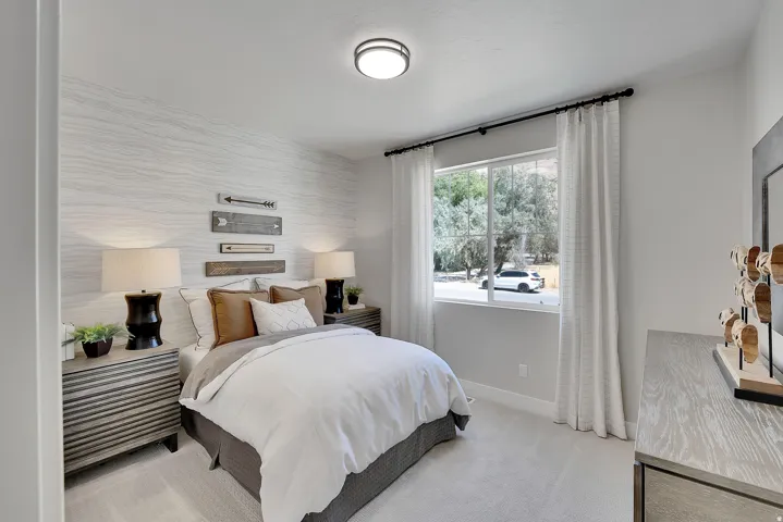 Carpeted bedroom featuring a large window with white drapes, a patterned accent wall, a flush-mount ceiling light, and light-toned walls